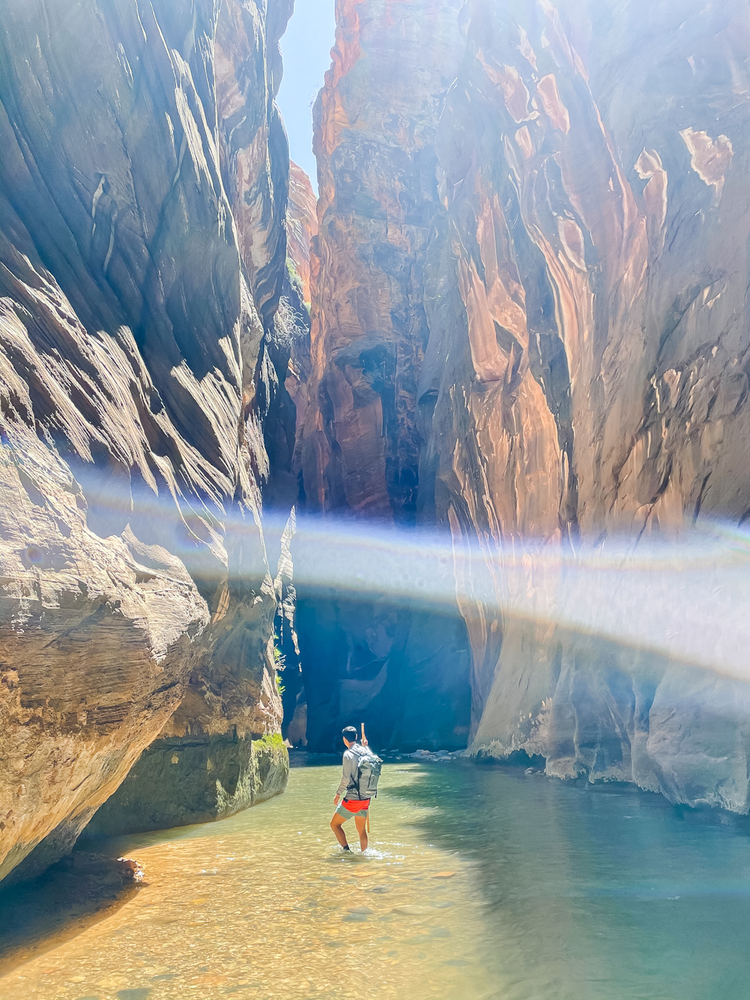 A man stands in the river amongst narrow canyon walls 