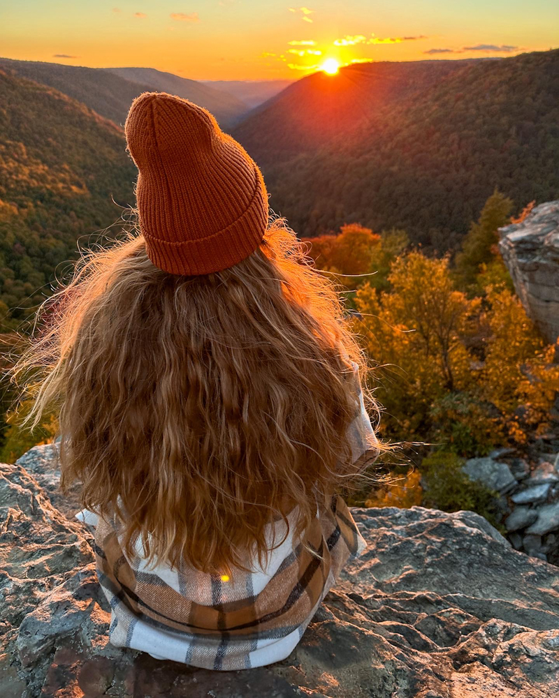 A girl sitting on a rock looking at the sunset in the valley