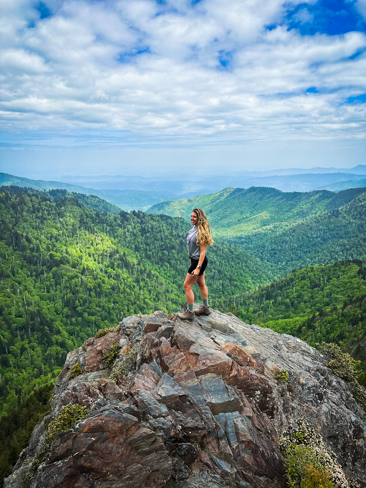 A girl standing on a rocky outcropping with mountains in the background