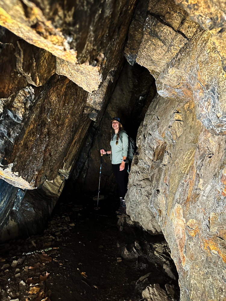 A girl stands at the back of a dark shalllow cave