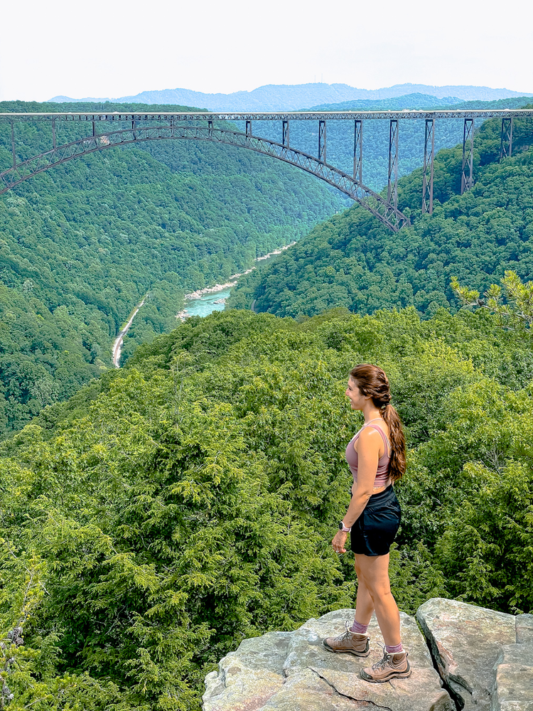 Girl standing on a rock with a view of New River Gorge Bridge