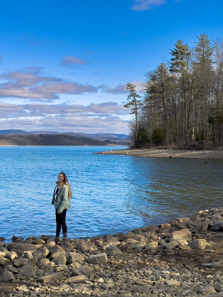 A girl stands along the shore of a lake 