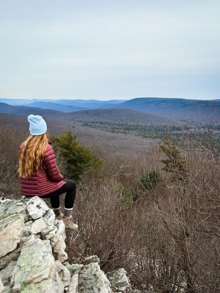 A girl sits on a rock ledge overlooking mountains