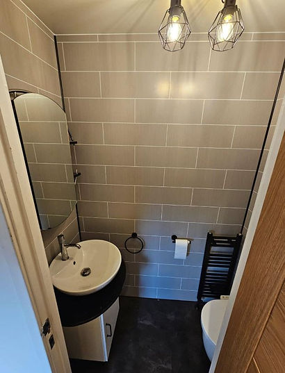 Small modern bathroom with gray tile walls, a round mirror, white sink, and black fixtures