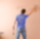 A man in a blue shirt smooths a freshly painted peach wall with a trowel