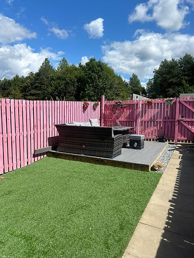 A vibrant garden oasis features a pink wooden fence and a cosy black wicker seating area