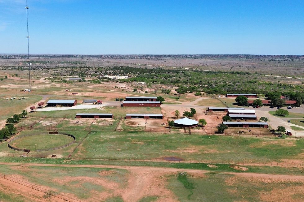 Vue aérienne d'une ferme avec plusieurs bâtiments rouges en plein désert. Ciel bleu dégagé et tour de communication visible au loin.