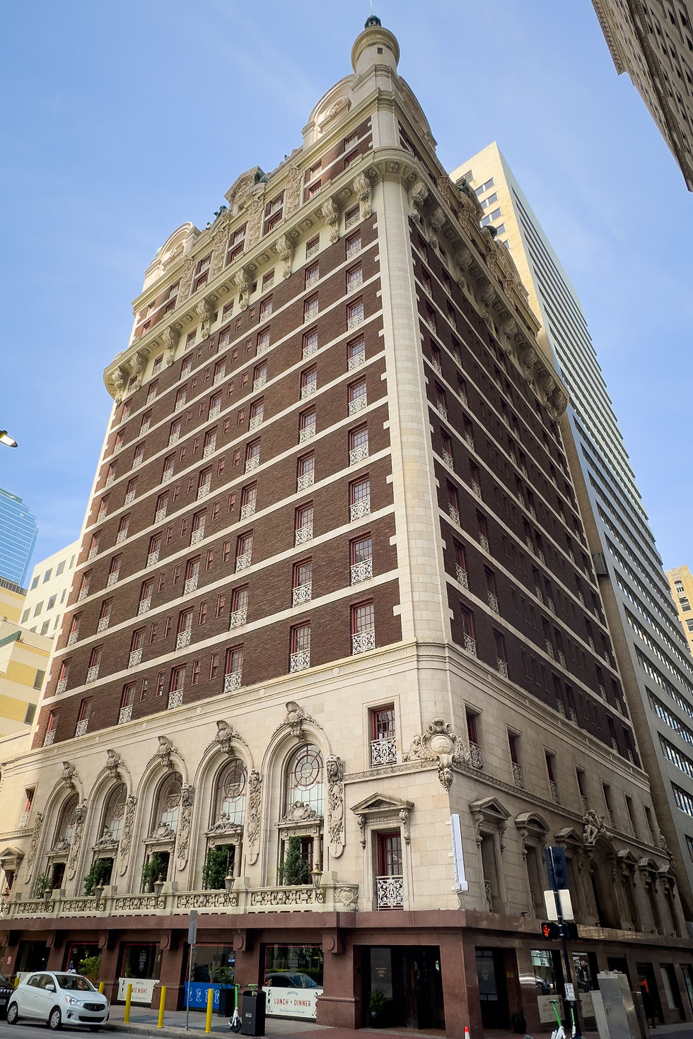 Immeuble historique en brique et pierre, de style architectural classique. Ciel bleu en arrière-plan. Voitures garées devant l'entrée.