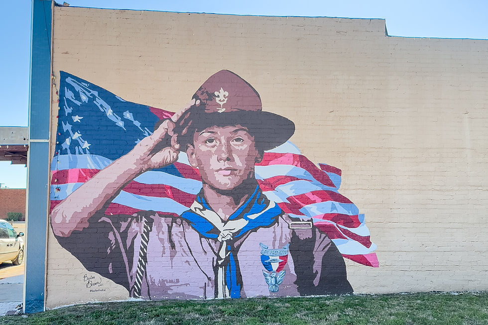 Fresque sur un mur montrant un jeune scout saluant devant un drapeau américain. Fond beige, couleurs vives, texte illisible en bas.