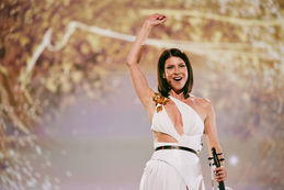 Moldova's 2024 Eurovision artist Natalia Barbu performs onstage in a white jumpsuit holding a violin