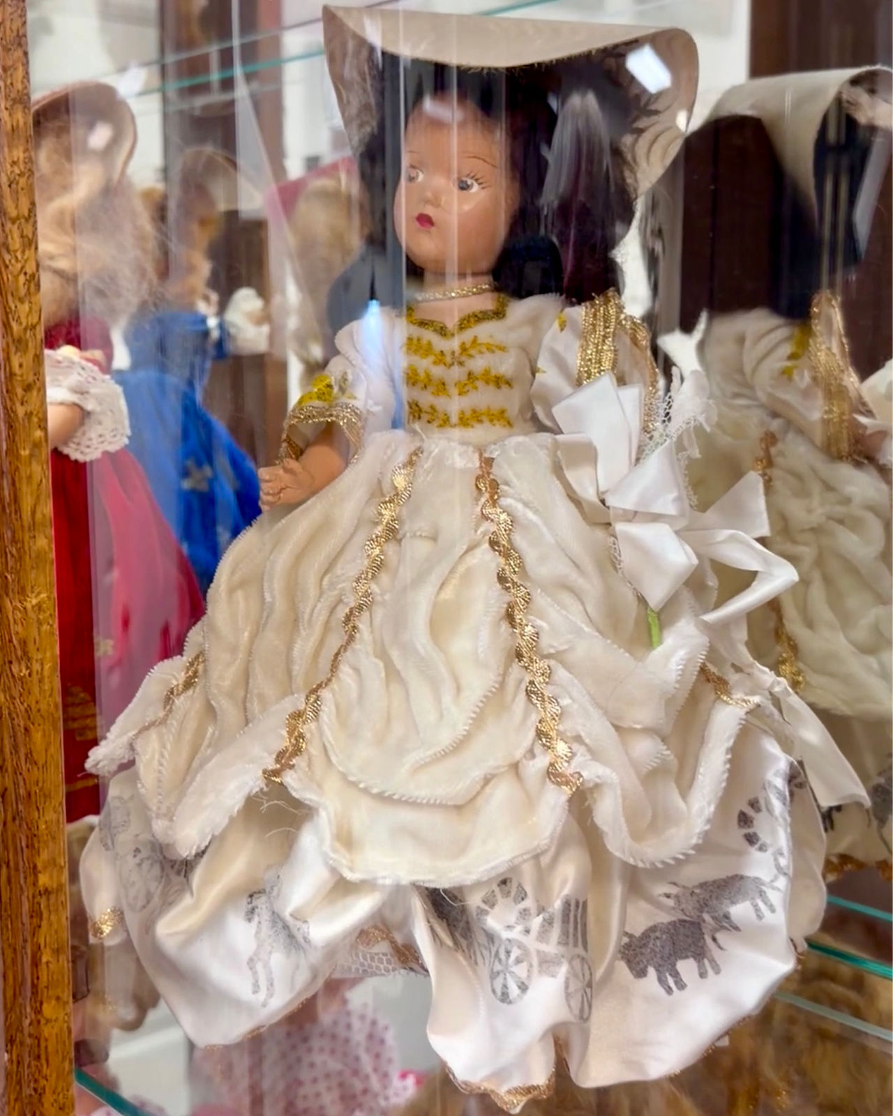 A 1947 Utah Centennial Day Doll wearing a cream-colored gown with gold trim and a border depicting o
