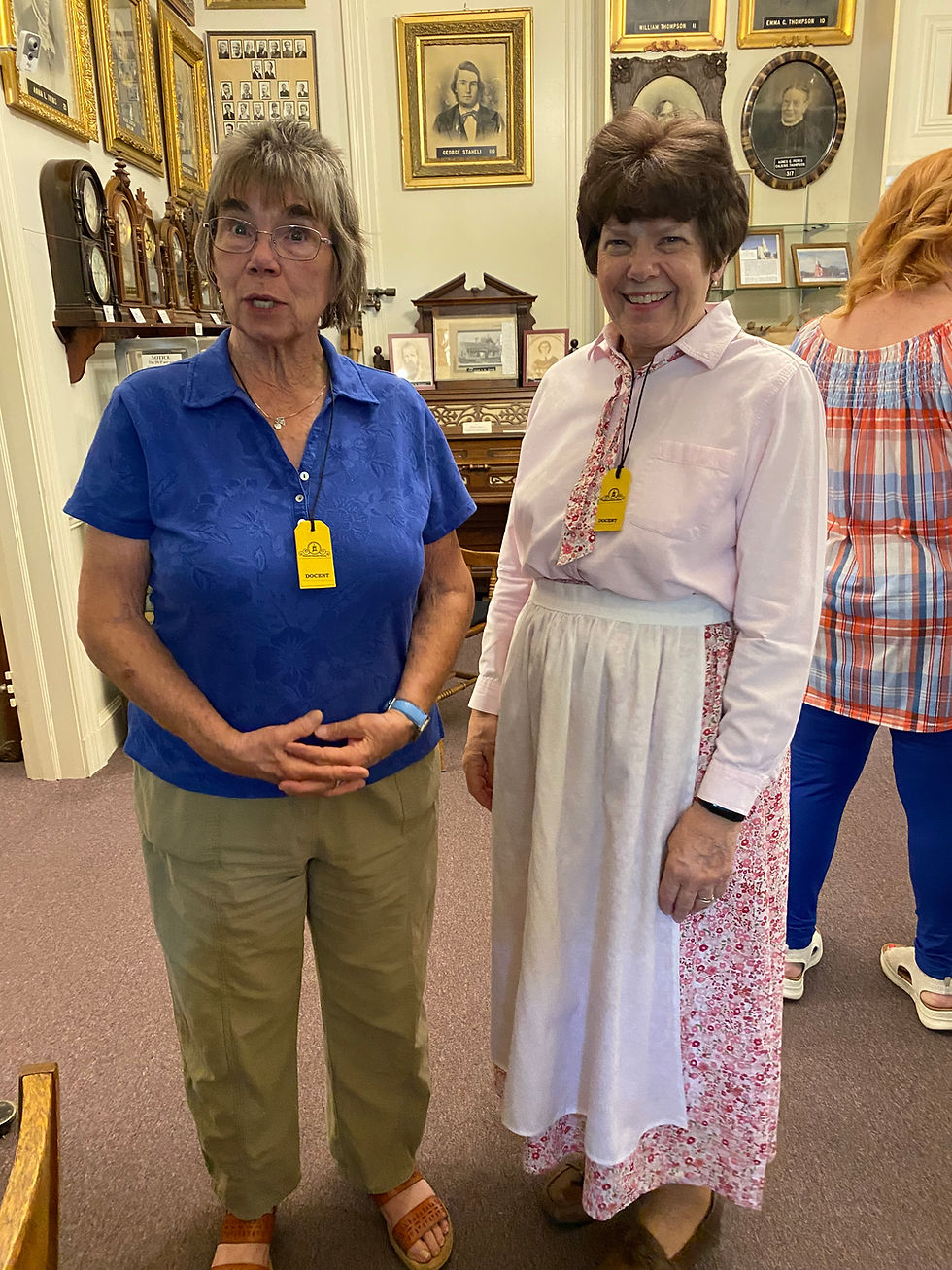 Two McQuarrie Memorial Museum docents in the exhibit area, one smiling and the other speaking to visitors.