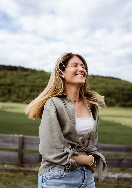Frau steht entspannt in der Natur und lacht – symbolisiert Leichtigkeit, Erdung und natürliche Coaching-Atmosphäre