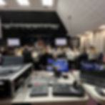 A table full of livestreaming equipment in front of a room full of people attending a conference