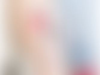 Photographie en gros plan d'un tatouage d'art corporel minimaliste et unique sur le biceps d'une personne, représentant deux chardons noirs stylisés à longues tiges et un soleil rouge texturé décentré. L'encre a une texture artistique et granuleuse. L'arrière-plan montre une chemise à fines rayures floue.