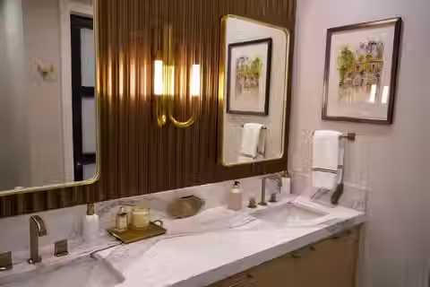 A white bathroom vanity with copper or bronze colored walls and two mirrors