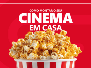 Banner de capa horizontal em fundo vermelho decorado com uma moldura branca retangular. Na parte superior, destaca-se a frase em letras garrafais brancas: "MONTE O SEU CINEMA EM CASA", posicionada logo acima de um balde listrado de vermelho e branco repleto de pipoca doce.