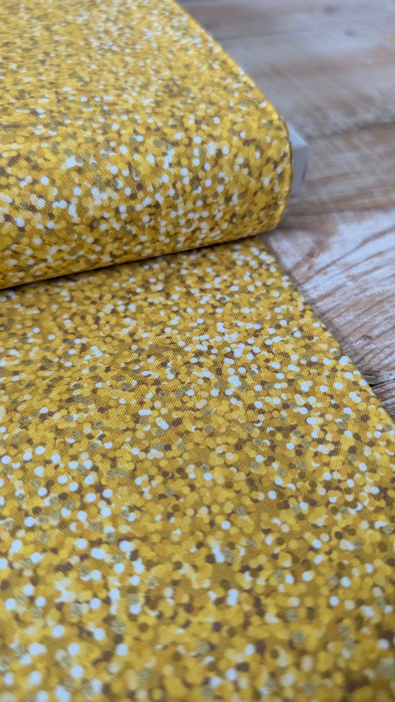 Thumbnail: Yellow fabric with white dots rolled out on a wooden table for sale.