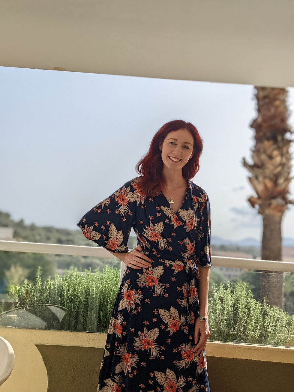 Thumbnail: Woman wearing floral dress smiling with arm on hip, standing outdoors, sunny day.