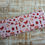 Thumbnail: Fabric with red patterns including birds, cherries and hearts on light pink.