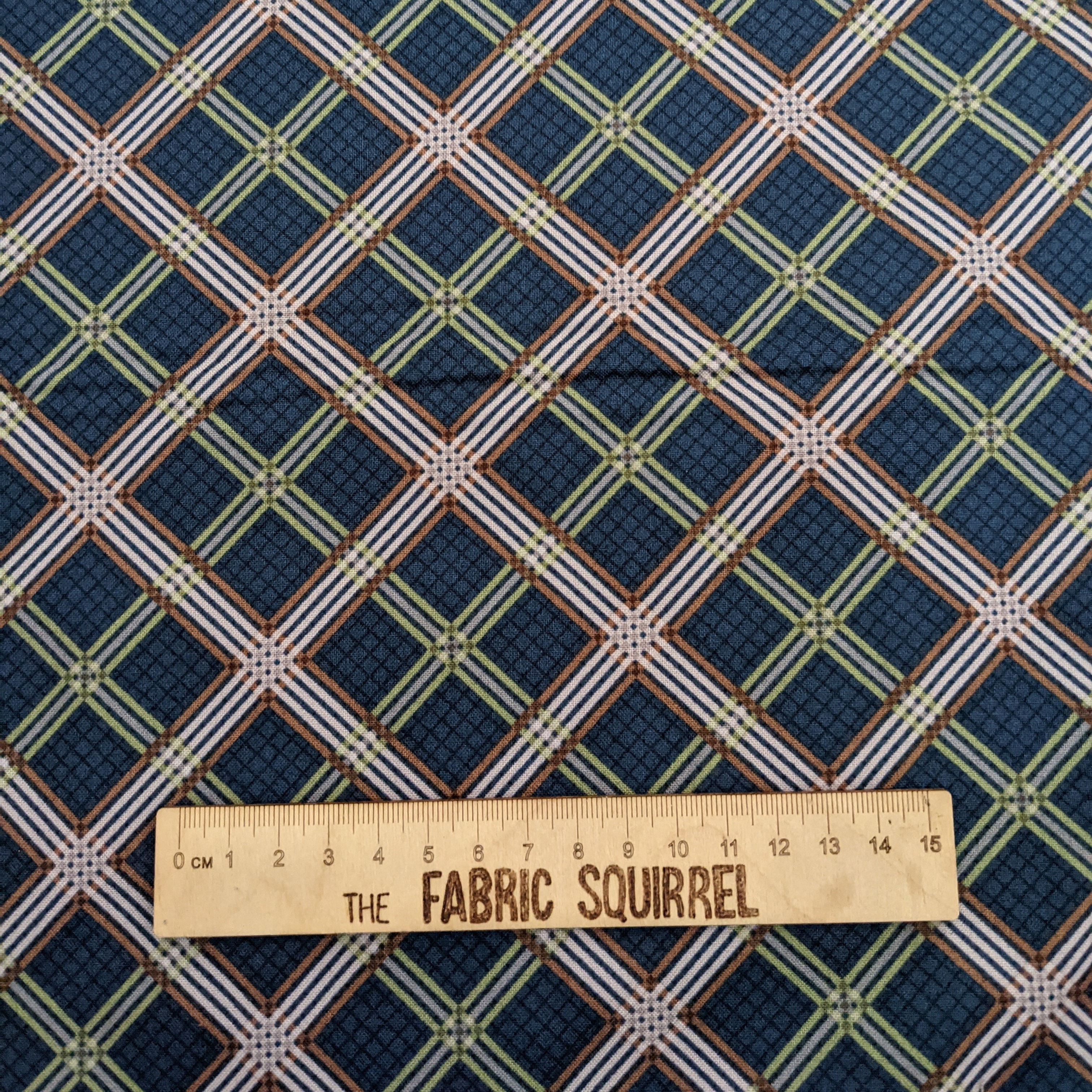 Blue fabric with white and brown lines and words The Fabric Squirrel, on ruler