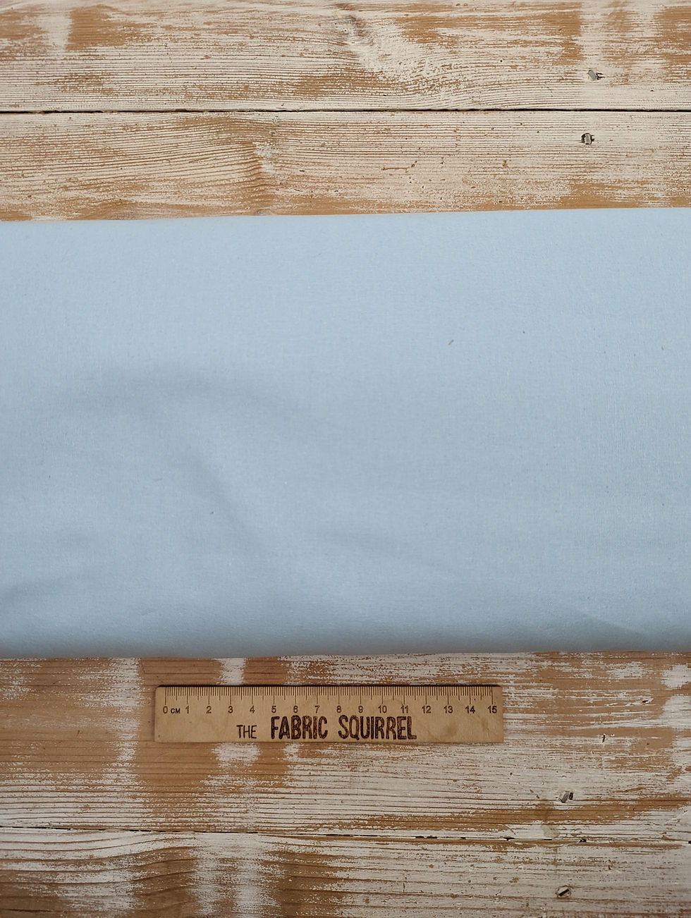 Thumbnail: Light blue fabric and ruler with text, The Fabric Squirrel, on wooden surface.