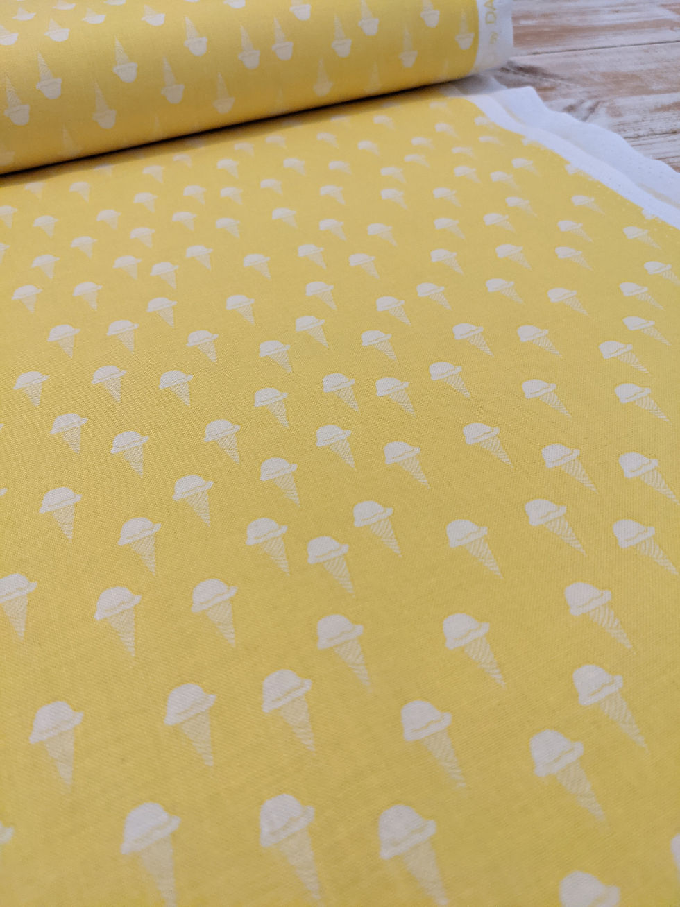 Yellow fabric printed with white ice cream cones, a whimsical design on display.