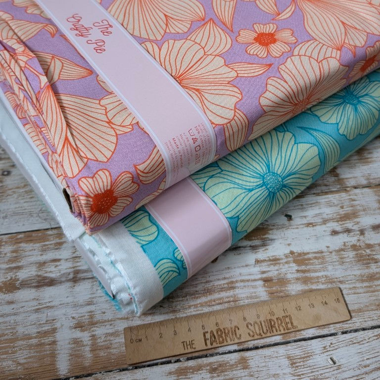 Thumbnail: Floral fabric rolls with branded ribbons and ruler on wooden surface. The Fabric Squirrel.