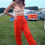 Thumbnail: Woman in orange pants and polka dot top posing near orange VW bus.