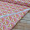 Thumbnail: Pink fabric with repeating fan design on a wooden surface backdrop.