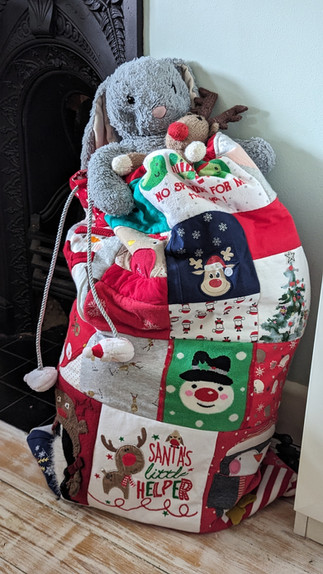 Christmas gift sack made from baby clothes filled with toys sat by a fireplace