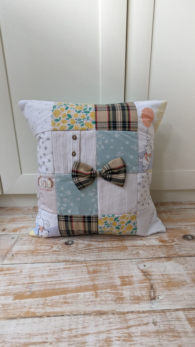 Thumbnail: 16 patch keepsake cushion made with girls baby clothes. Finished off with a bow taken from one of the dresses.