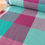 Thumbnail: Rolled fabric displaying a checkered pattern of teal, pink, and purple colors.