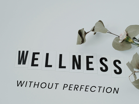 The word WELLNESS spelled out in black letters on white cards, next to a sprig of dried eucalyptus with a single small white flower.