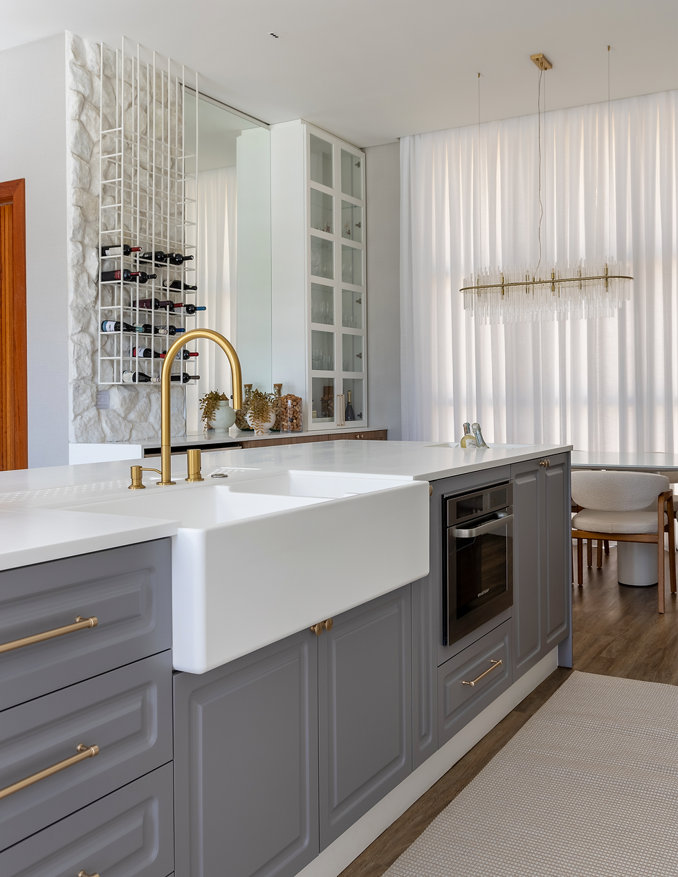 Detalhe da cozinha com armários brancos com portas de vidro, bancada em Durasein Glacier White, vaso com flores cor-de-rosa e parede em mármore com iluminação suave.