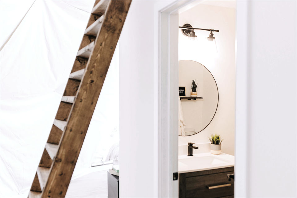 Rustic wooden ladder beside white canvas leading to modern bathroom vanity.