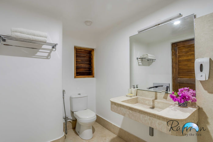 White bathroom with handmade marble sink, toilet, and wooden-framed window.