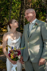 The bride smiles and looks longingly at the groom while he speaks. They are holding hands.