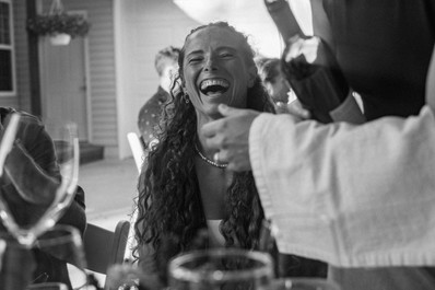 A guest laughs while being poured wine during dinner in black and white.
