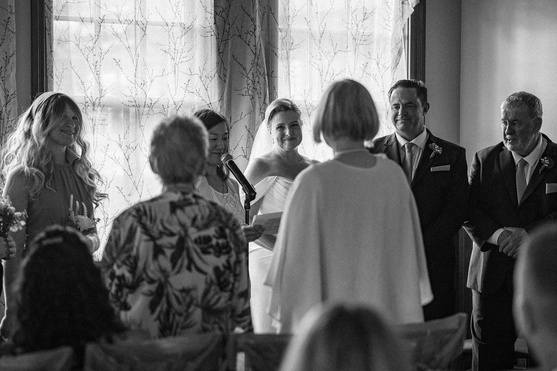 The bride and groom listen to the officiant speak during the ceremony. In black and white.