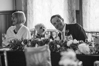 The groom smiles at the camera posing with the dog at eh table. In black and white.