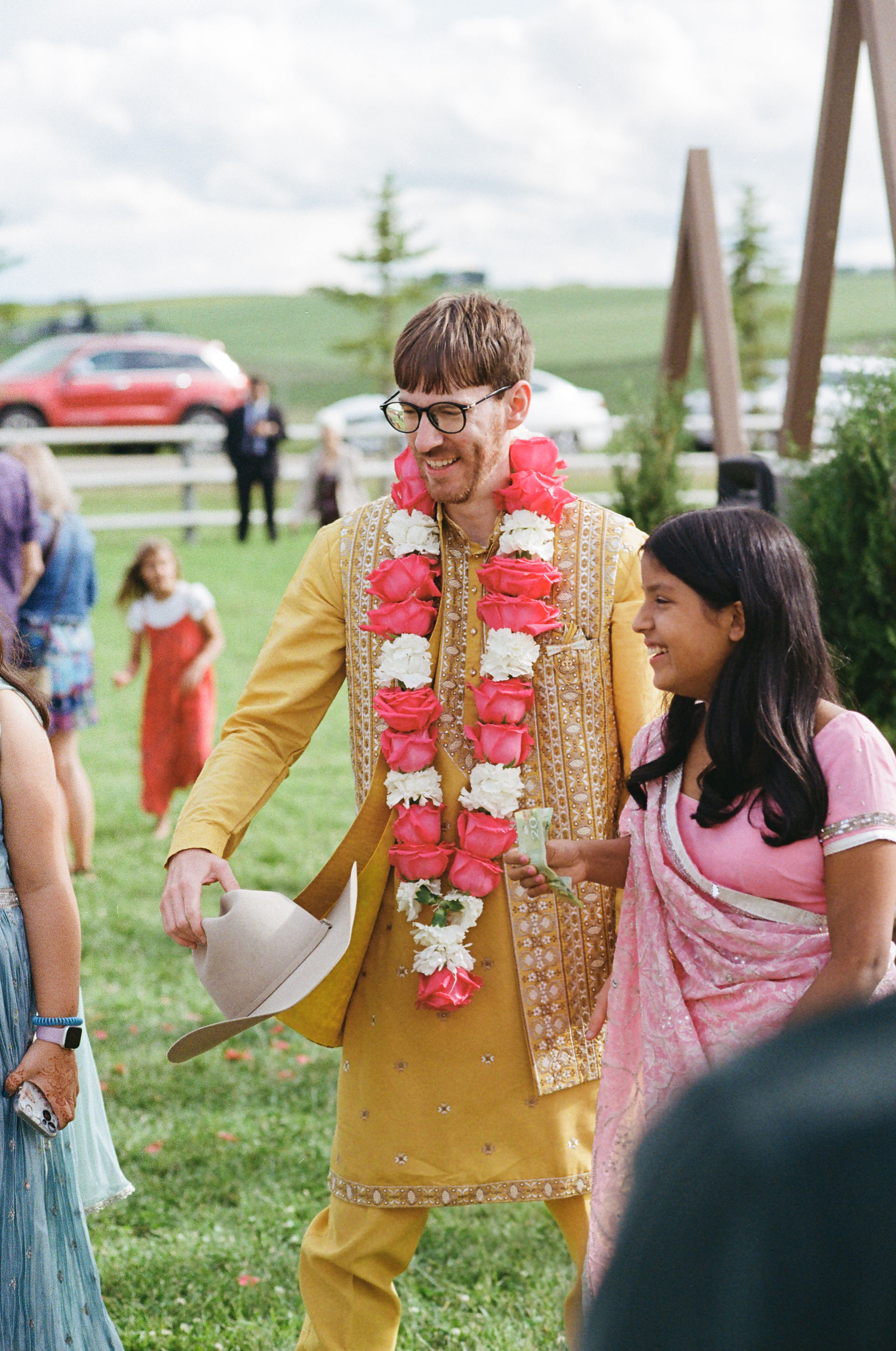 The groom stands with the brides sisters, holding a cowboy hat dressed in his sherwani.