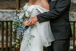 The groom embraces the bride from behind while she holds her bouquet.