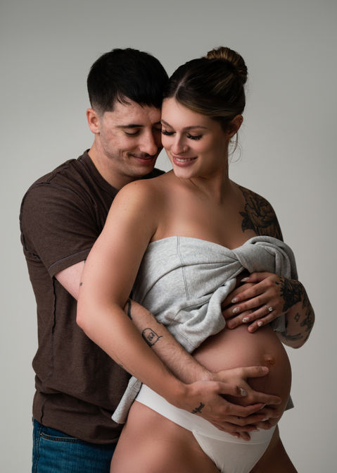 Modern studio Maternity Photography in Falmouth, Maine with photo of a pregnant woman posing in with man hugging her