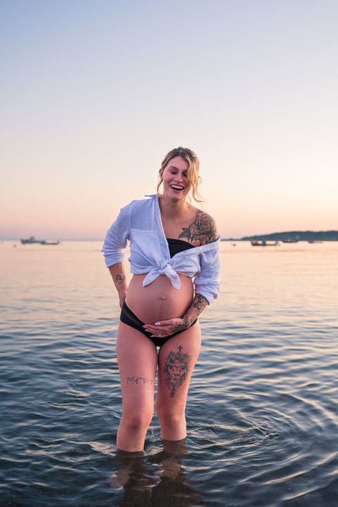 Beach Maternity Photography in Cape Elizabeth, Maine with photo of a pregnant woman in the water with bikini and white beach top
