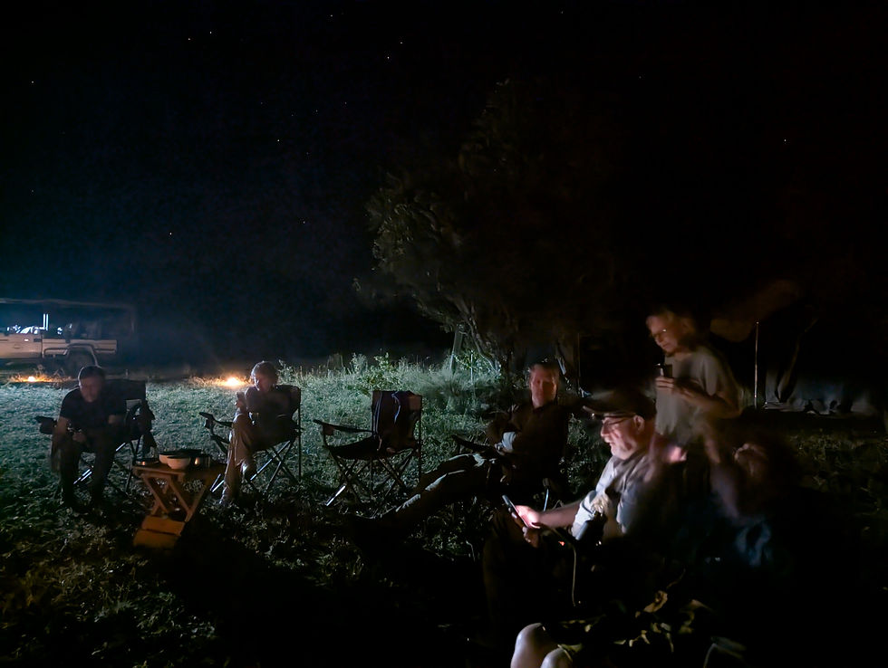 Campers sit in folding chairs around a fire at night under a starry sky, with a tent and vehicle in the background.