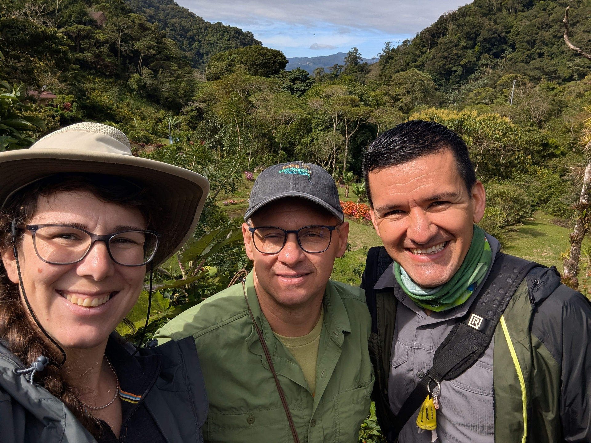 Three people smalling with lush mountain valley in background.