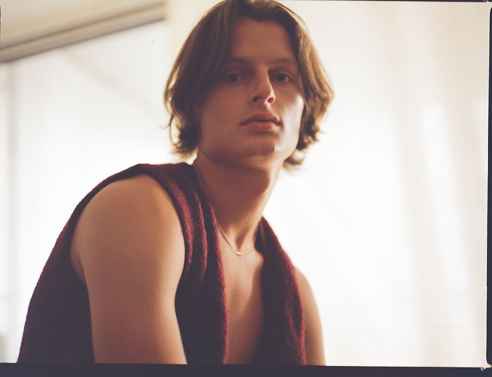 Close-up portrait of a young person with brown hair and a maroon sleeveless top, gazing calmly against a bright white background.