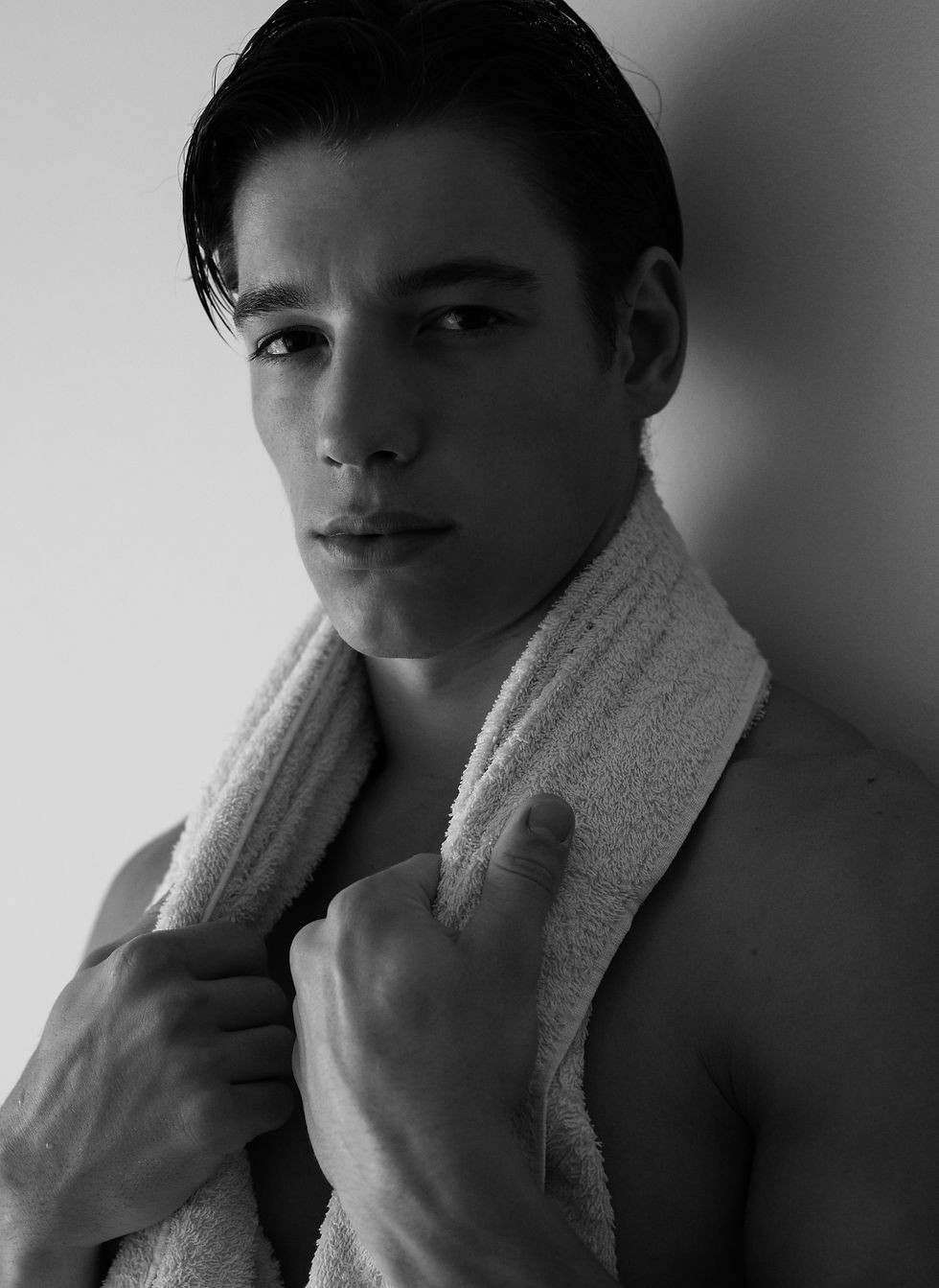 Retrato en blanco y negro de un joven serio con una toalla al cuello, mirando a cámara sobre fondo liso.