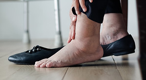 close up of an older person's feet, one shoe off and one on, bare foot is obviously causing pain
